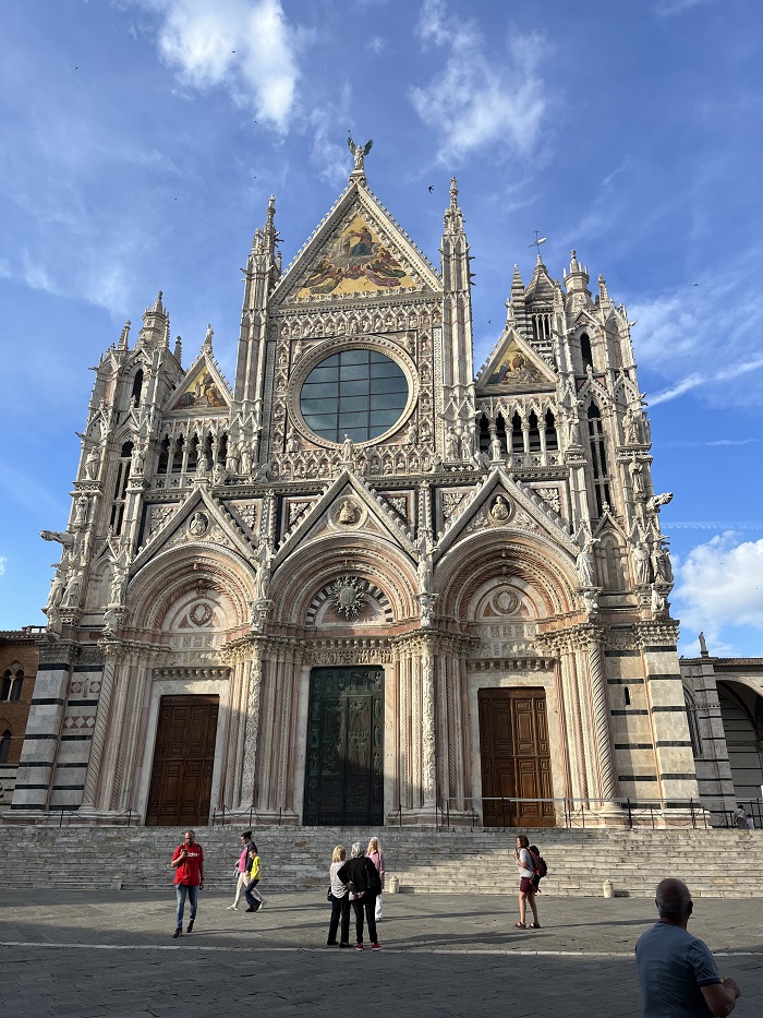 The exterior of the Duomo di Siena in Italy with seven people walking in front of the building