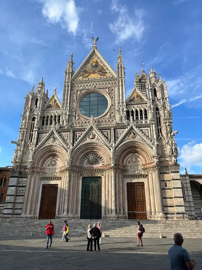 The exterior of the Duomo di Siena in Italy with seven people walking in front of the building