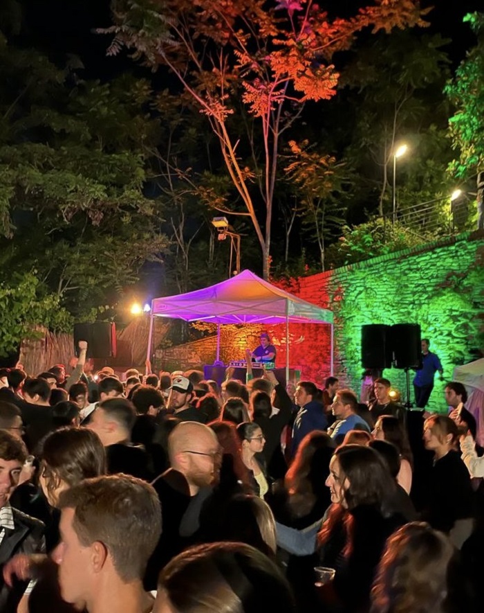 Many people crowded in an outdoor space with neon lights lit up in Italy
