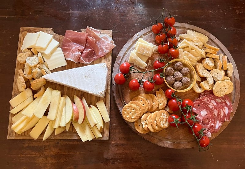 Tomatoes, meats, cheeses, and fruits displayed on two charcuterie boards on a table