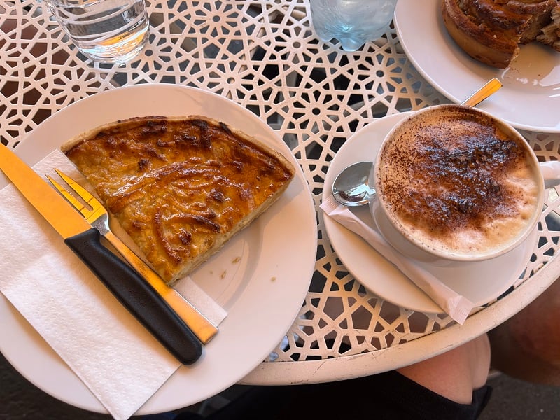 A slice of Swiss apple pie alongside a cappuccino on a table in a café 