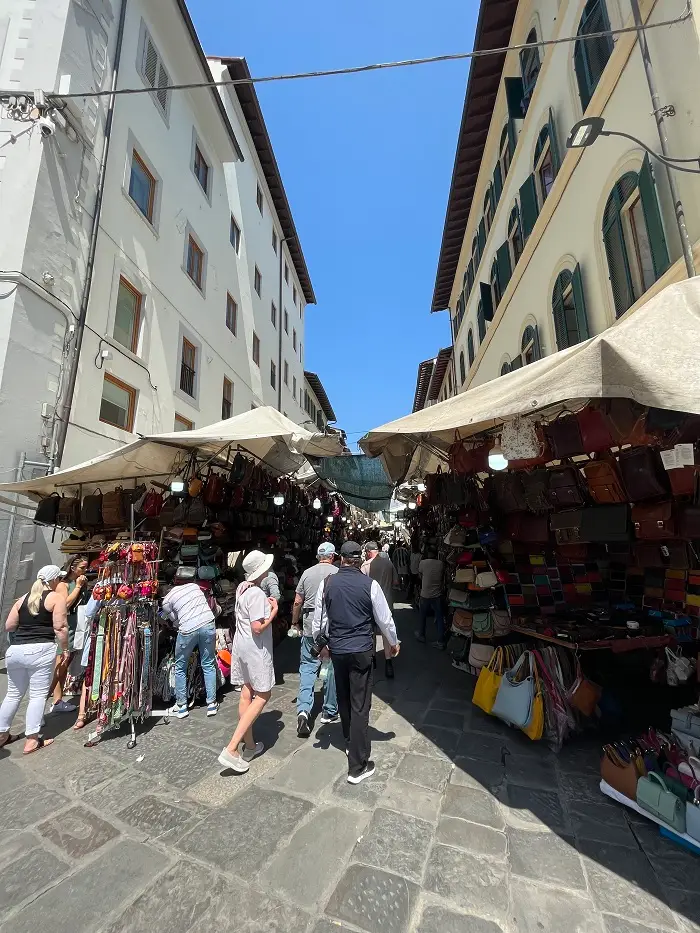 People standing under tents of vendors selling Florentine commodities, like primarily leather bags and wallets in Italy