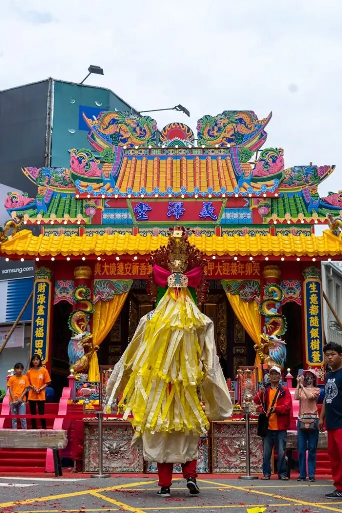 A person standing in front of a temple in a costume for the Dajia Mazu Pilgrimage festival held in Taiwan