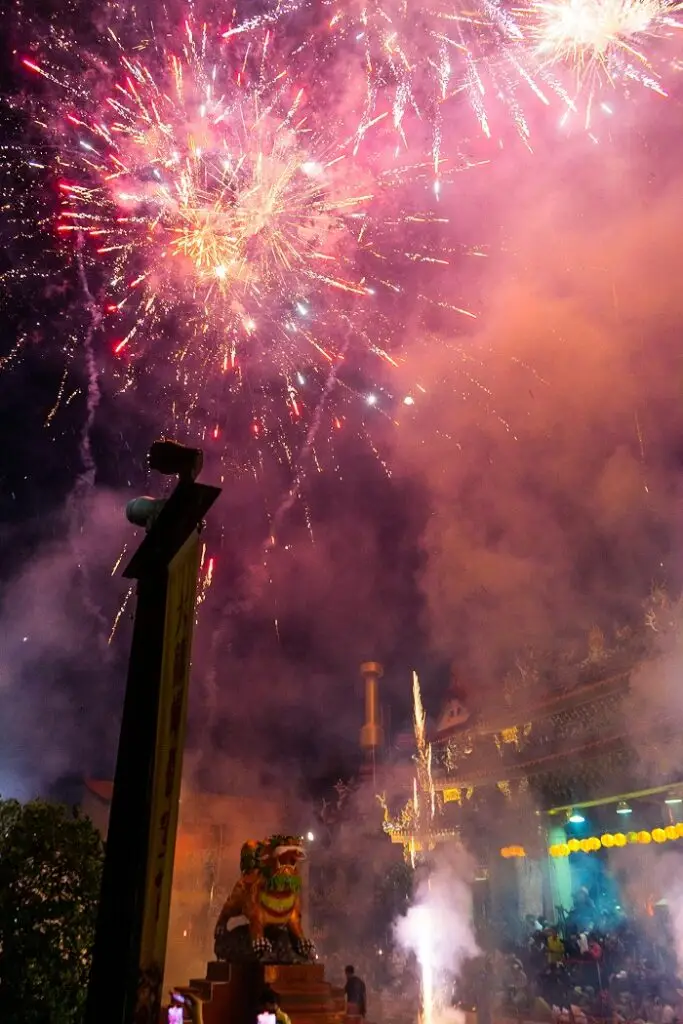 Large fireworks in a smokey atmosphere at the Dalongtong Bao’an Temple for the Baosheng Cultural Festival. The temple is packed with people making offerings and burning incense.