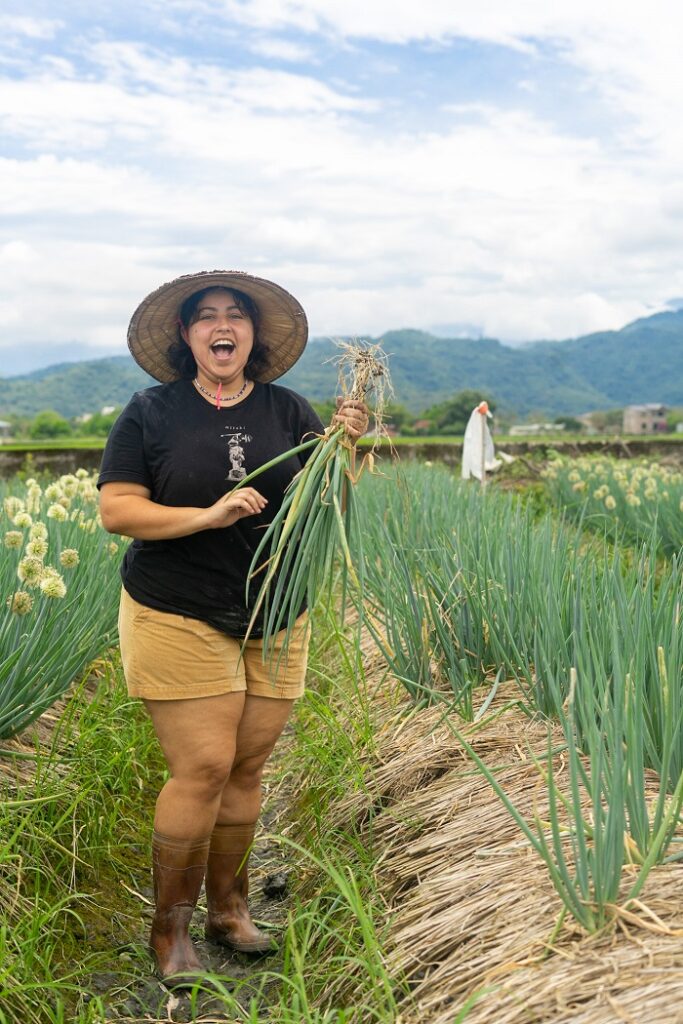A CET Taiwan roommate standing in a field of scallions and holding up some scallions she picked in her hand