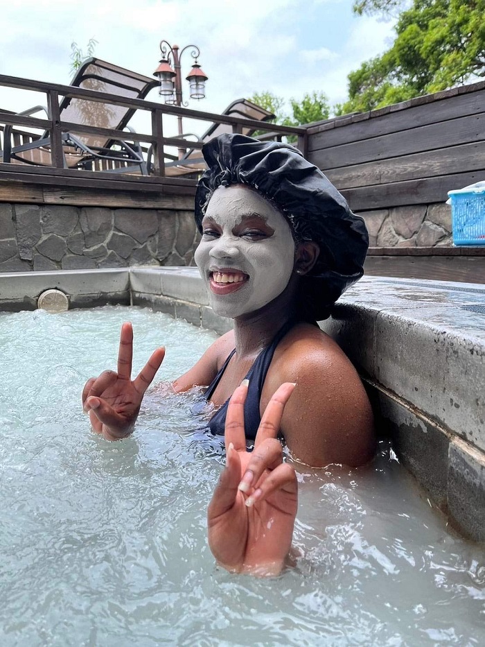 A CET Taiwan student smiling with peace signs up and sitting near the edge of the outdoor Beitou Hot Springs with a face mask on