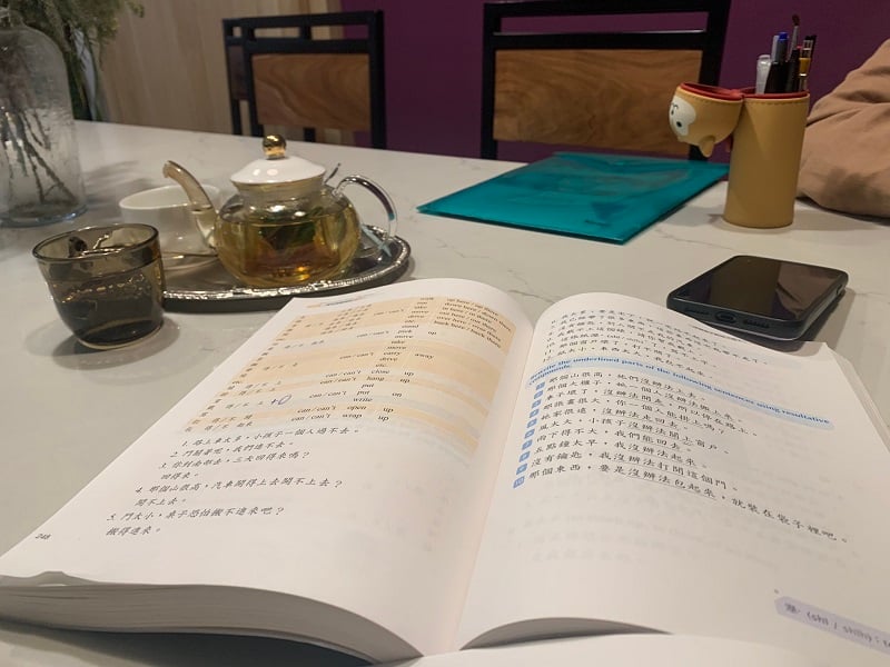 An opened traditional Chinese characters workbook alongside a pot and cup of tea on a table in Bona Café in Taiwan