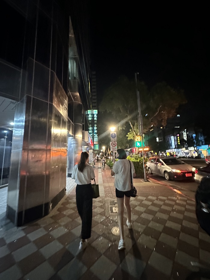 Two girls walking down the middle of a sidewalk at night in the city in Taiwan