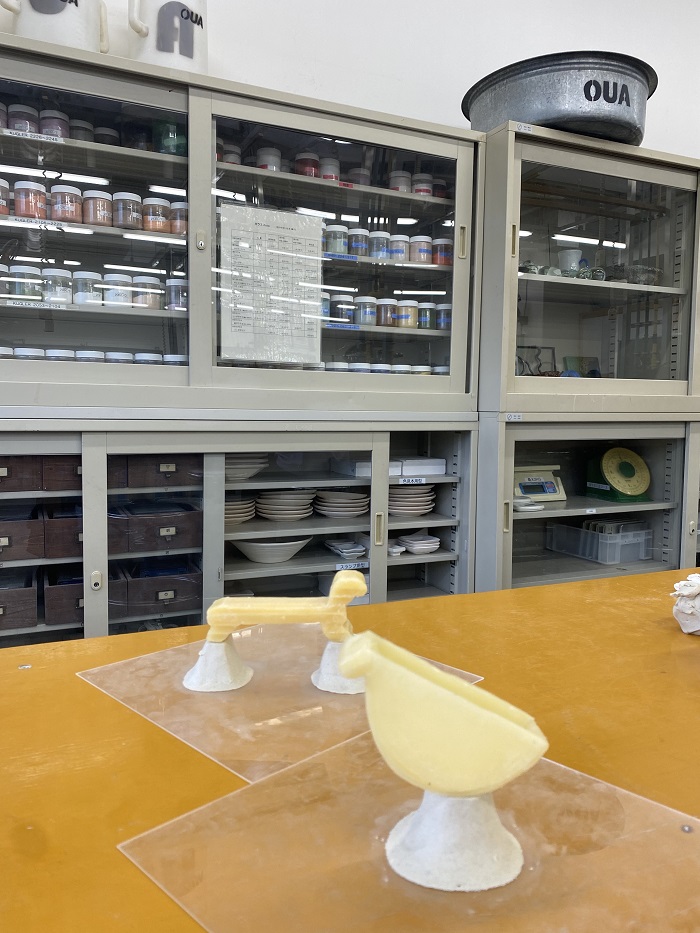 Two plaster molds on a table in a kiln casting class with paints and plates stored away in cabinets