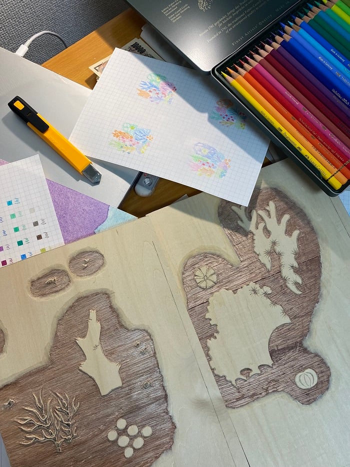 Paper with sketches, colored pencils in a tin, and a woodblock carved out in a printing class at AICAD in Japan