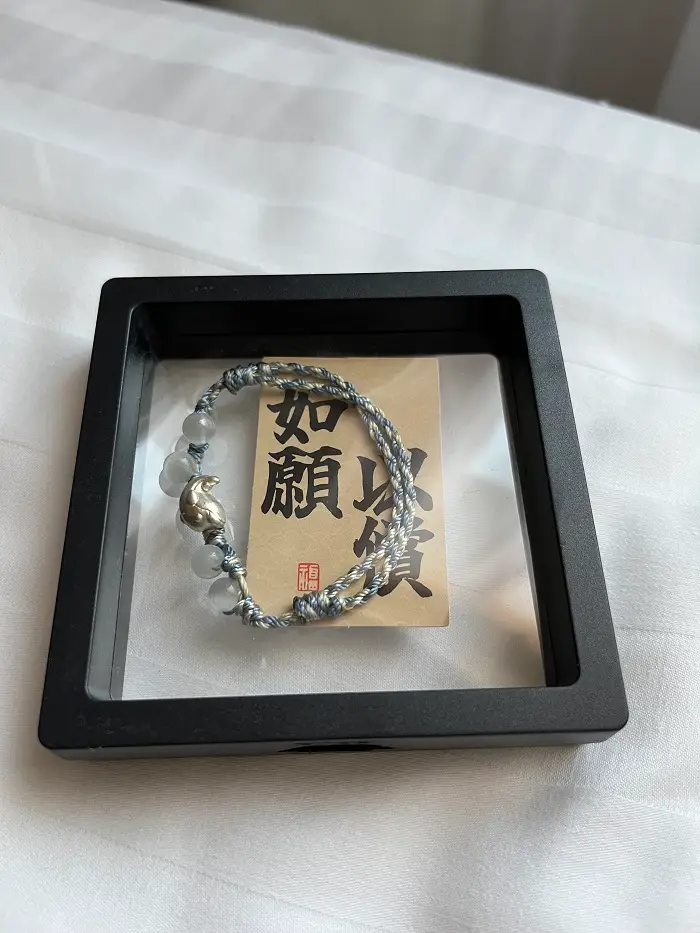 A close-up of a bracelet with a little fish in the middle and some opaque beads
