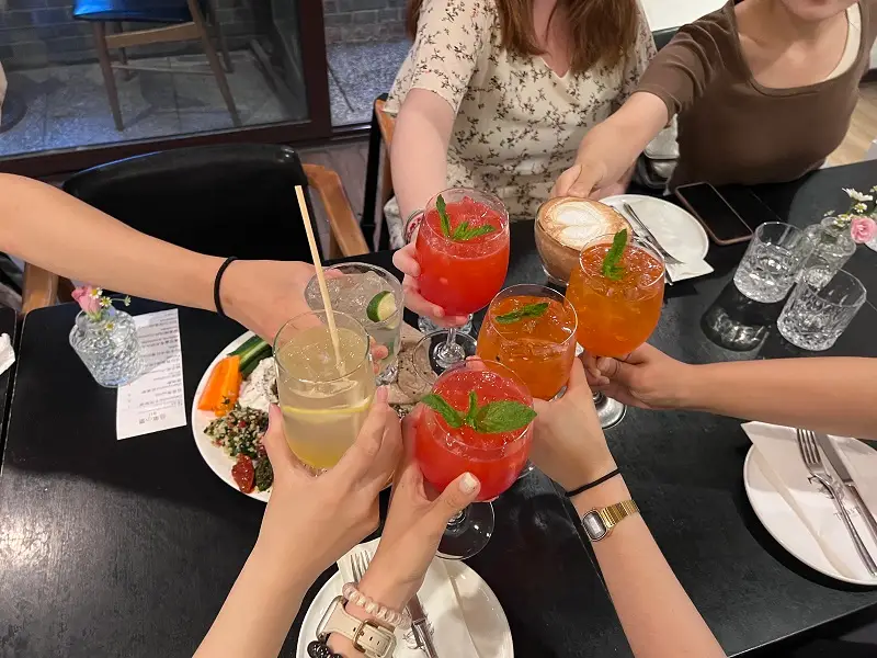 People holding up glasses of drinks gathered in the middle of the table for a cheers