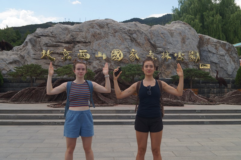 Two CET Beijing students imitating the Chinese character for mountain, 山, with their arms up at the base of a mountain