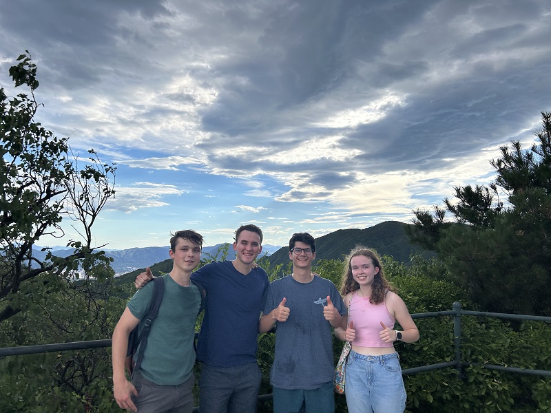 A group of four CET Beijing students smiling together at the top of Fragrant Hills Park surrounded by greenery and partly cloudy skies in Beijing