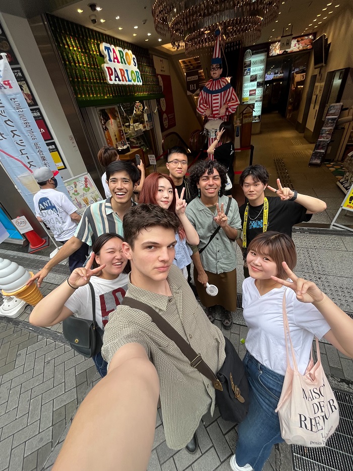 A group of CET Japan students and their roommates posing by a sculpture of a boy playing the drums in pajamas in Dotonbori