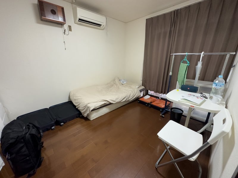 A room with a bed in the corner, chair, and small desk