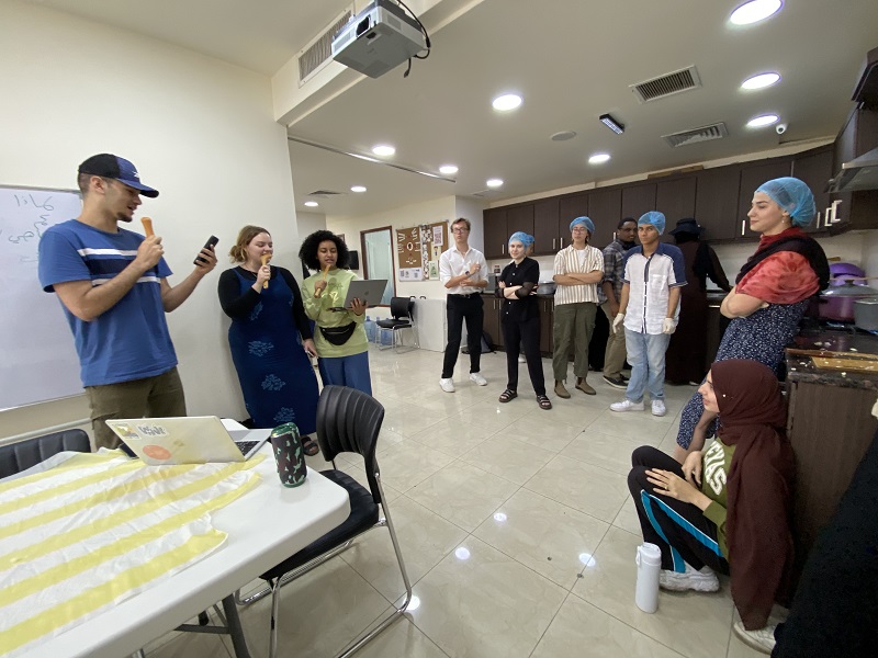 CET Jordan students standing around in a kitchen preparing to cook and three students singing on the side