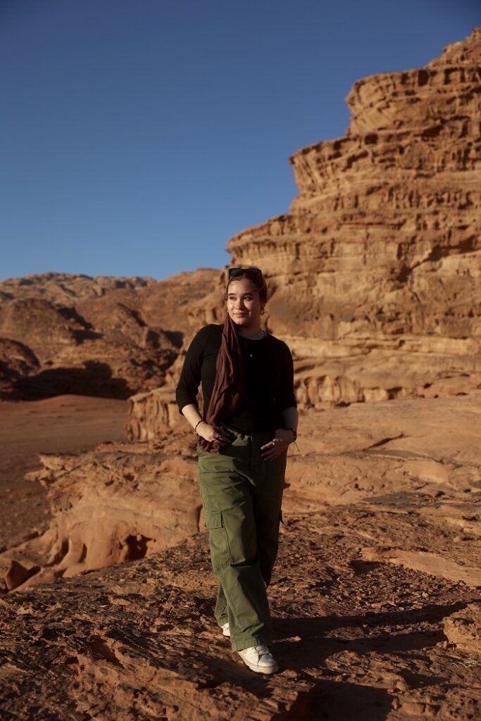 A CET Jordan female student posing with her hands in her pockets on a rock with the background of Wadi Rum
