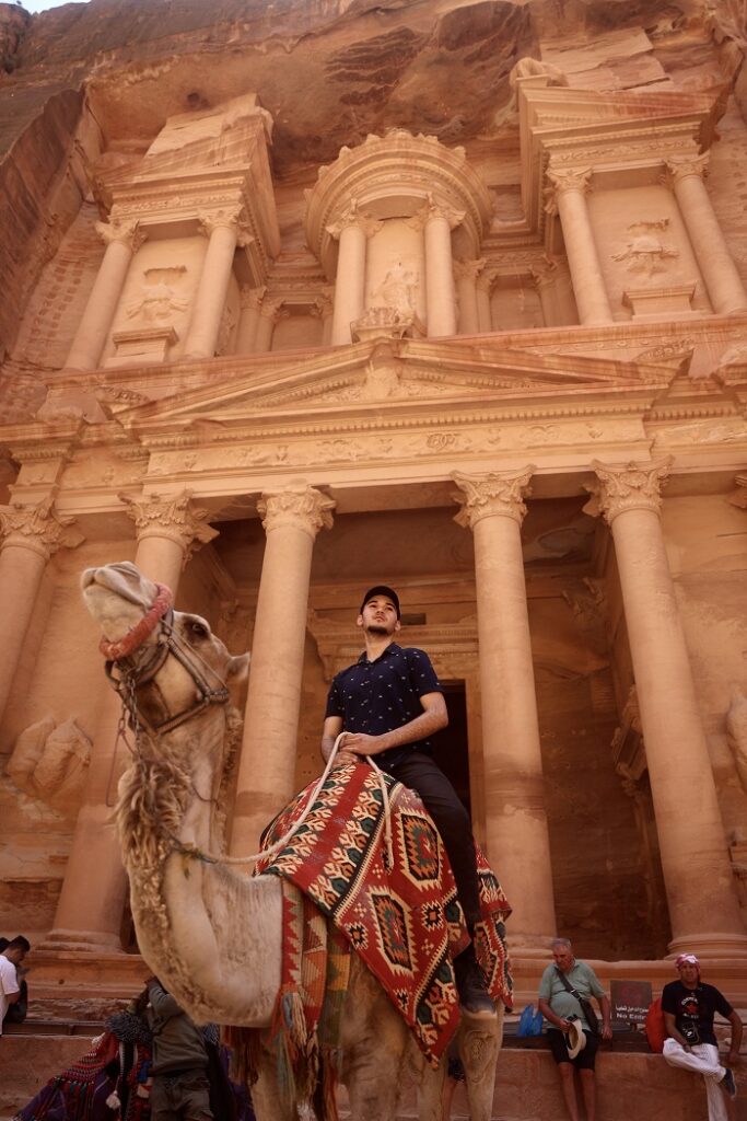 A male CET Jordan student sitting on the back of a camel looking into the distance while in front of Petra in Jordan