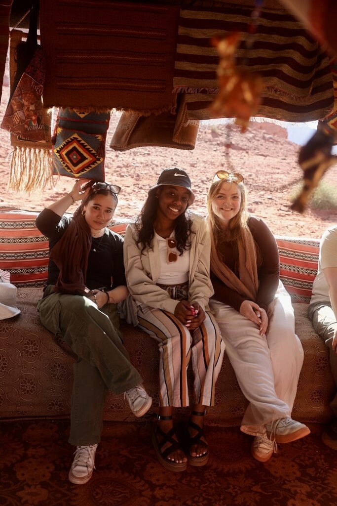 Three female CET Jordan students sitting under a woven tapestry on a sofa in the desert of Wadi Rum in Jordan