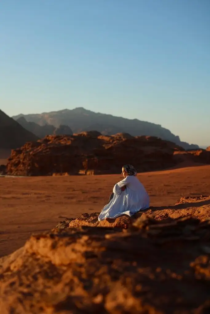 A female sitting on a large rock on a hilltop in Wadi Rum during sunset in Jordan