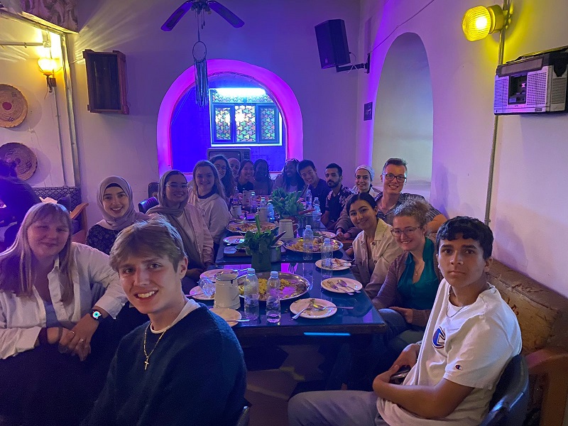 A large group of Jordanian neighbors and CET Jordan students around a table with food at a restaurant, Jameeda Khanum
