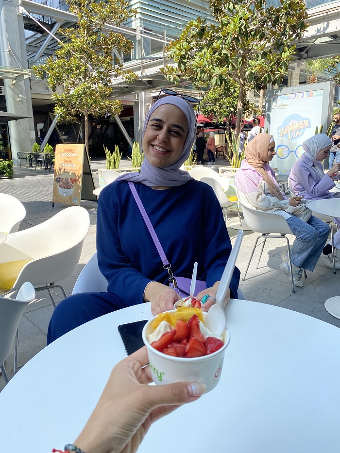 A CET Jordan language partner smiling while the photographer holds a cup of frozen yogurt with various fruits