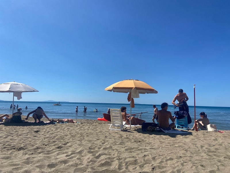 People sitting and laying under umbrellas at Castiglione della Pescaia in Tuscany on a bright clear summer day