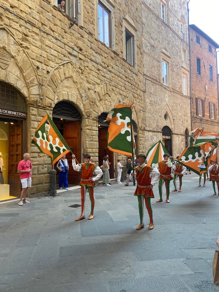 People waving flags in pairs along the streets within Siena in preparation for the Palio di Siena 