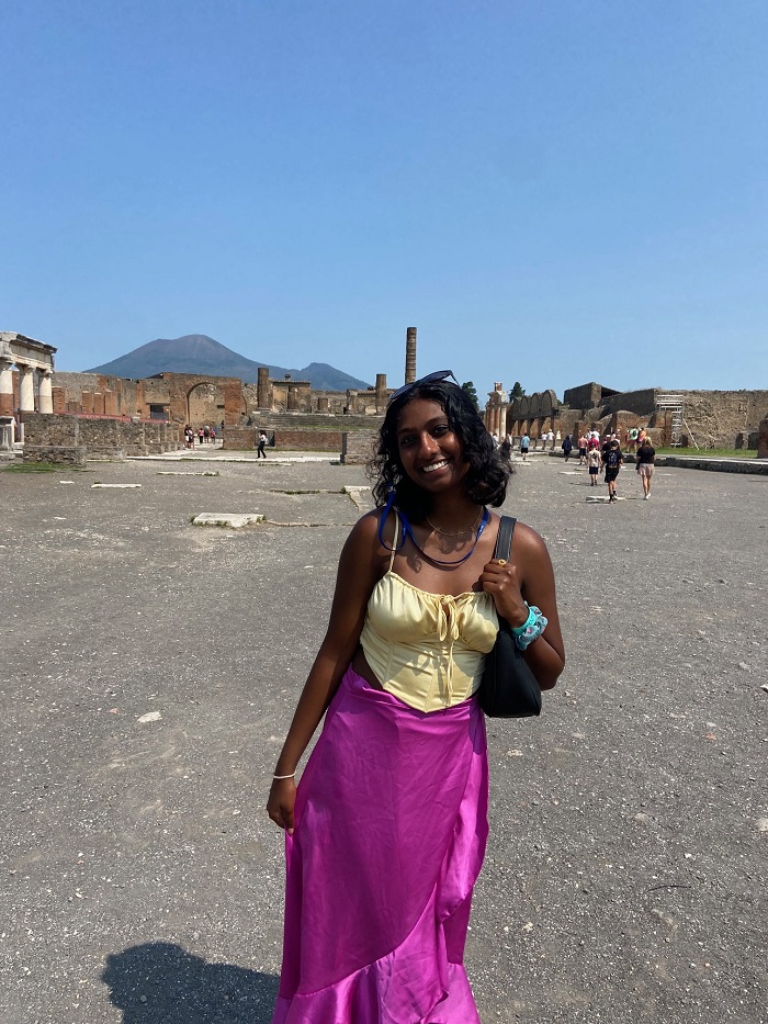 A CET Siena student smiling with the remains of Pompeii and other travelers exploring the grounds in the background