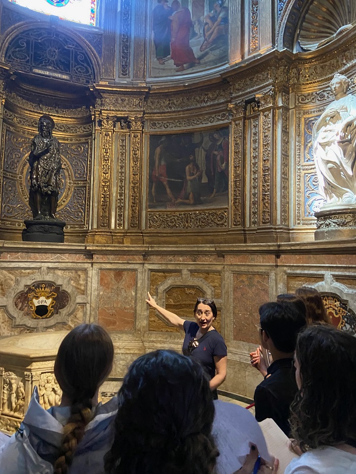 The back of students' heads and a professor pointing to a statue within the Siena Duomo 