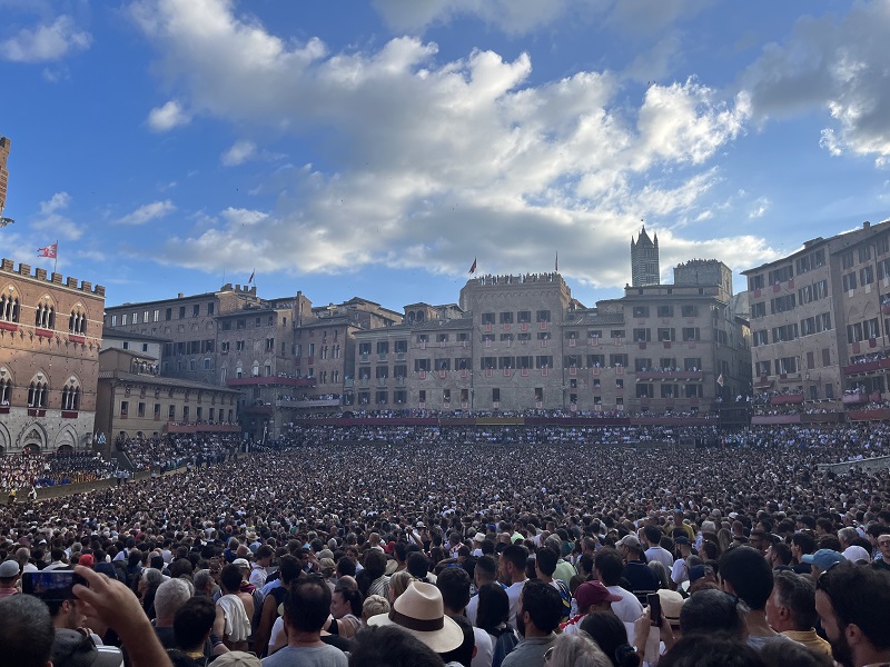 Piazza del Campo entirely filled with people awaiting the Palio di Siena on a partly cloudy day