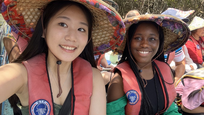 A CET Taiwan student and another girl wearing hats made of straw while sitting on a boat