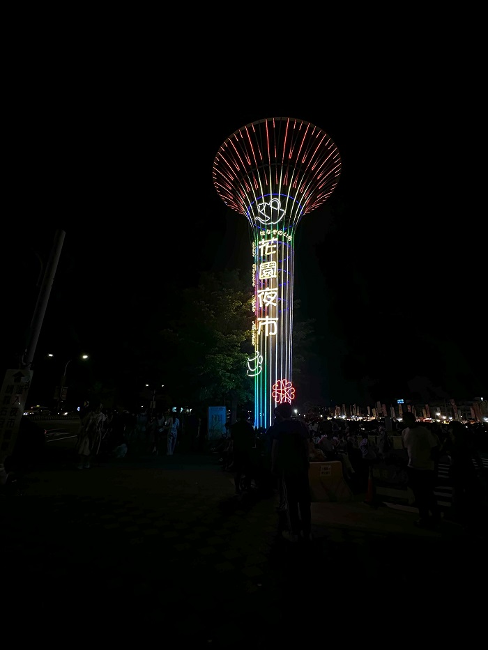 A tower with Chinese letters glowing in the dark by a night market in Tainan