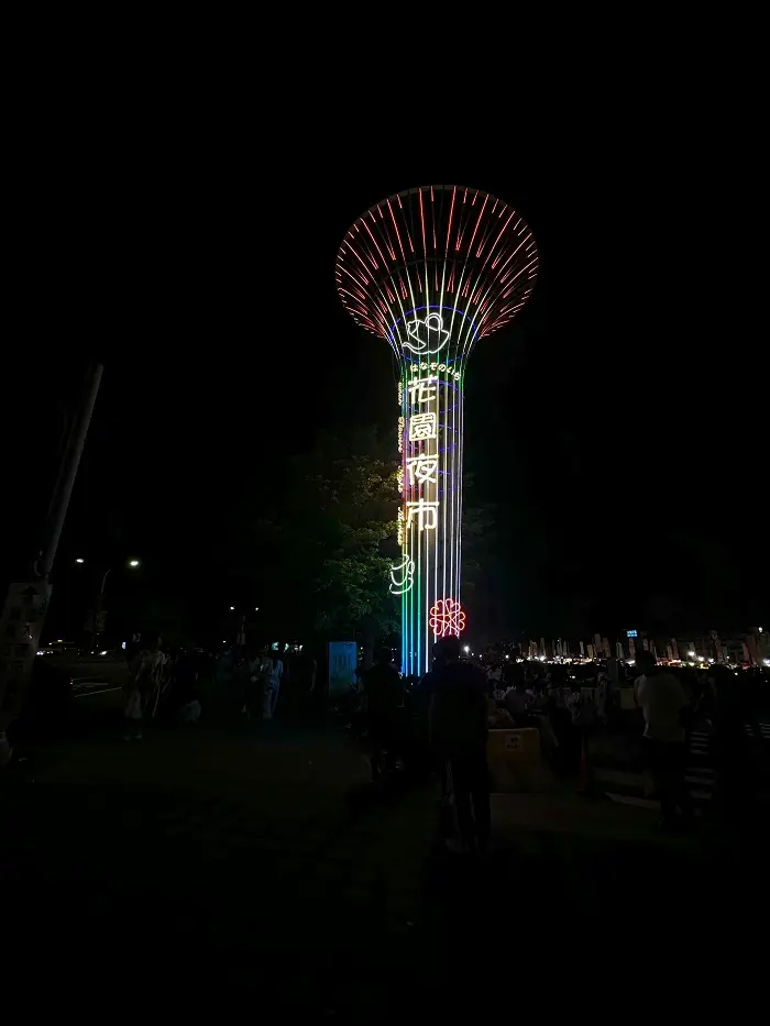 A tower with Chinese letters glowing in the dark by a night market in Tainan