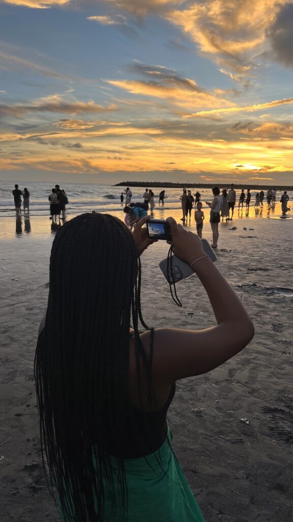 The back profile of a CET Taiwan student taking a photo of the sunset on a beach at Tainan with a small digital camera