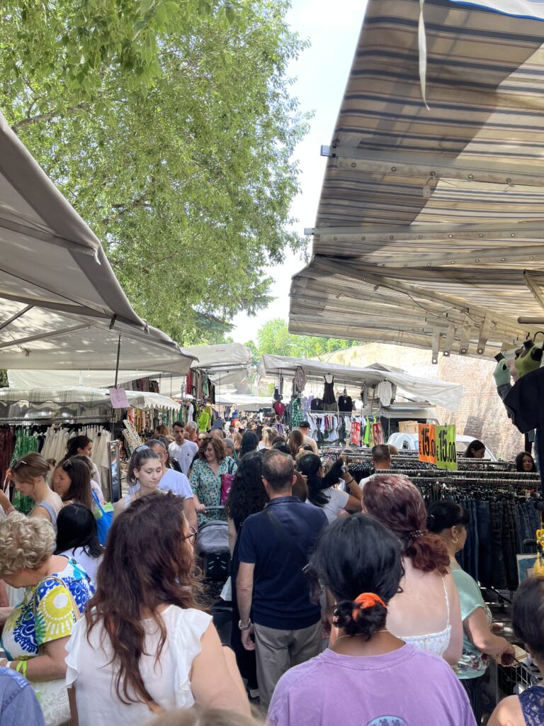 A aisle outside filled with people and vendors selling items on both sides in a market near Fortezza Medicea in Siena, Italy