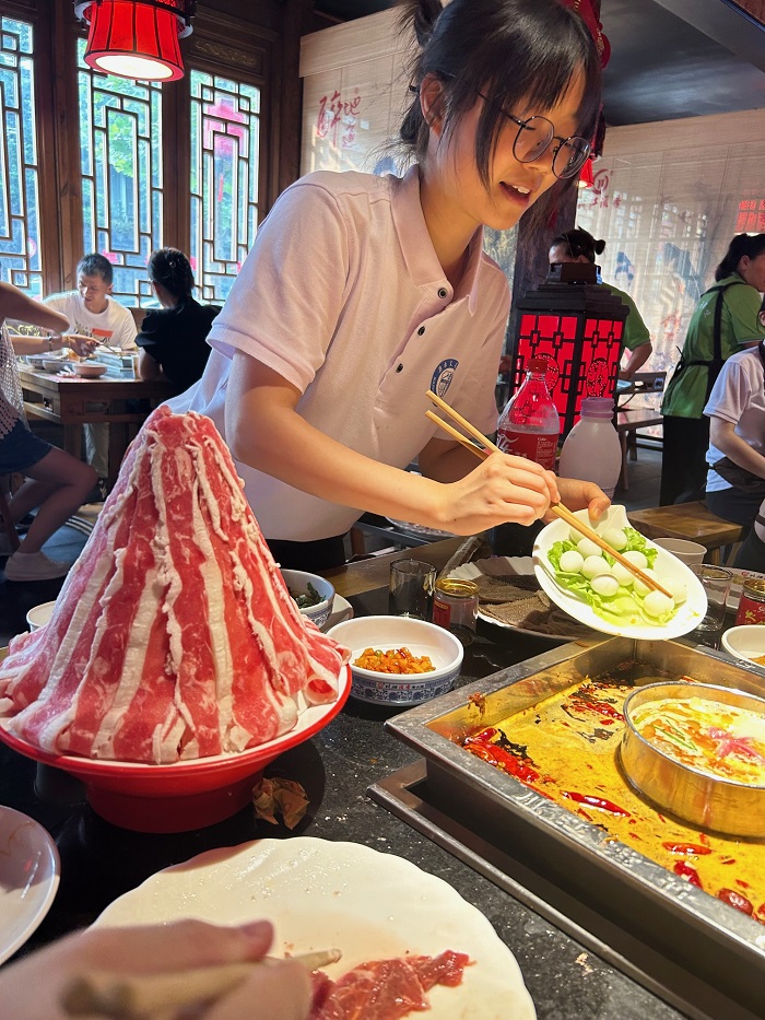 A CET Beijing language partner placing vegetables within a spicy Sichuan hot pot in a restaurant