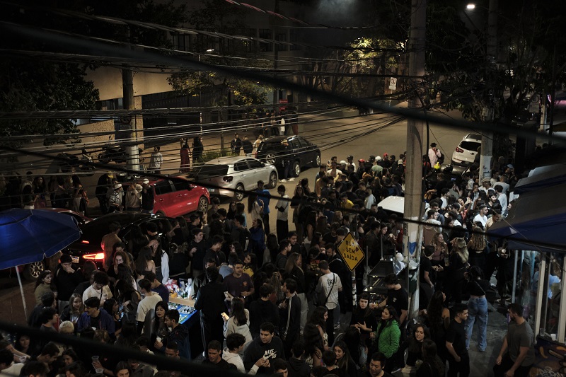 A large group of students gathered at the backside of Pontifical Catholic University of São Paulo at night for a block party