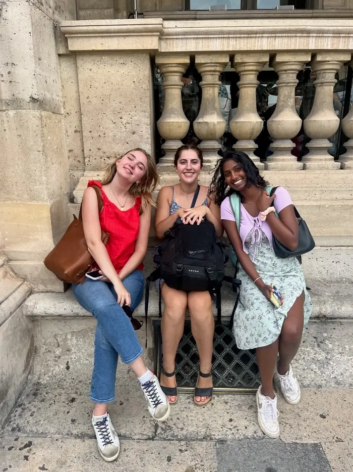 Three CET Siena students sitting along the edge of a building and smiling at the camera