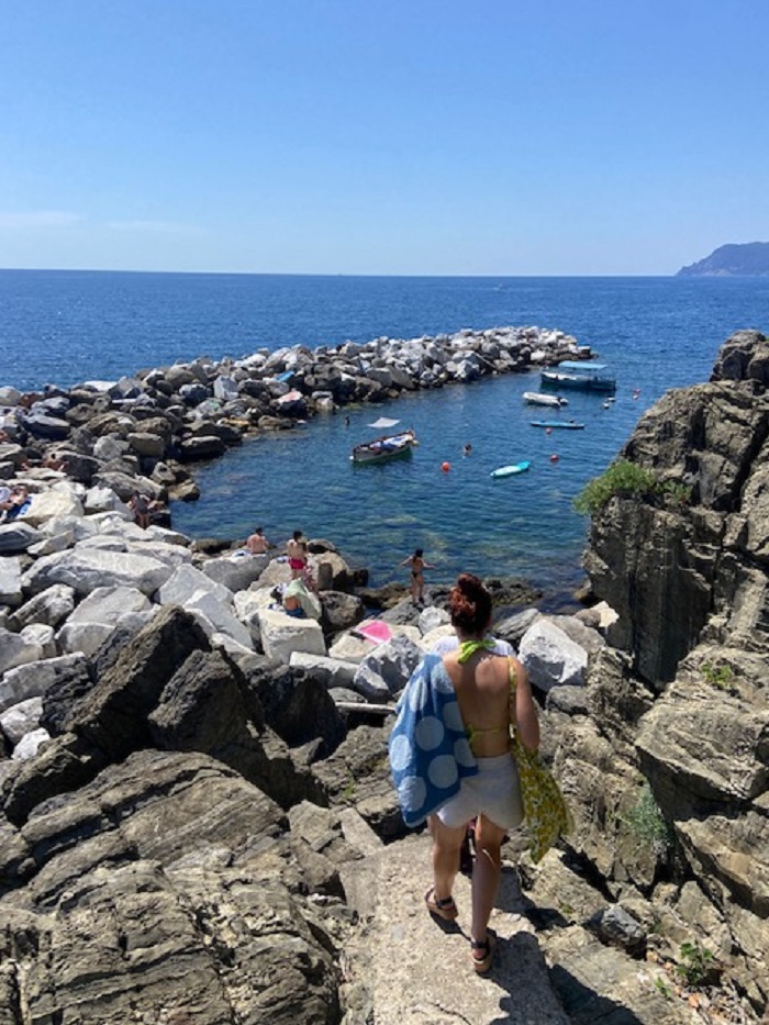 People on a rock beach by waters of Riomaggiore in Italy