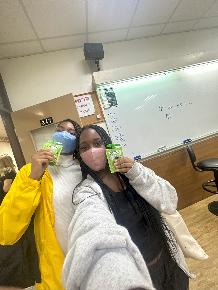 Two CET Taiwan students holding up apple sauce pouches in a classroom