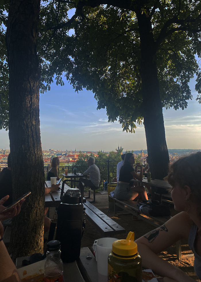People sitting outside on benches at Letna Park beer garden with the view of  the town in Prague, Czech Republic