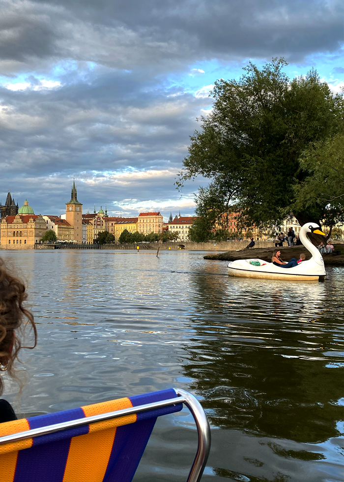 People paddle boating on the Vltava River on a partly cloudy day