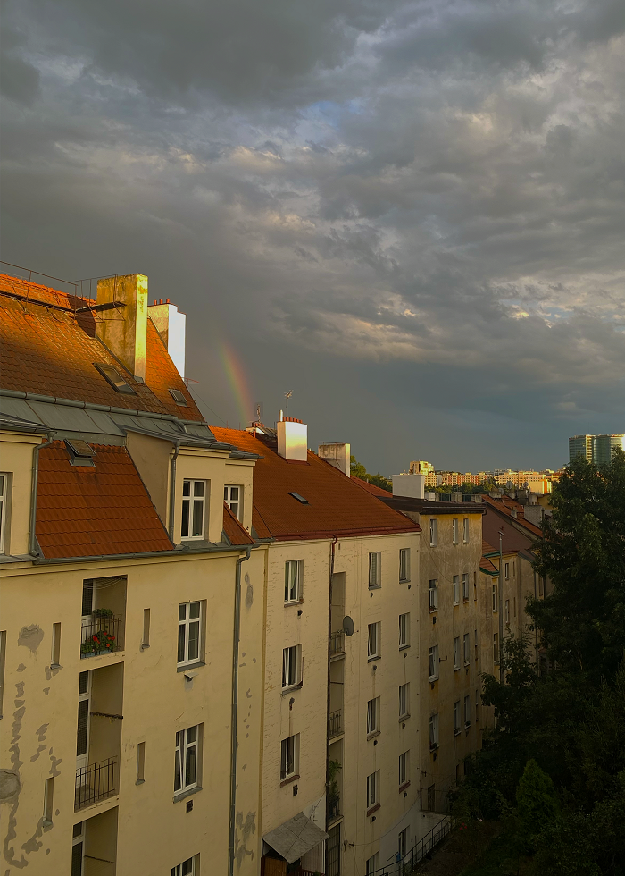 A little rainbow disappearing into the clouds and behind an apartment  building in Prague
