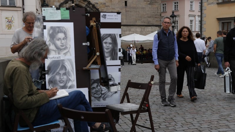 An artist sketching portraits of people and people passing by the artist in Prague, Czech Republic