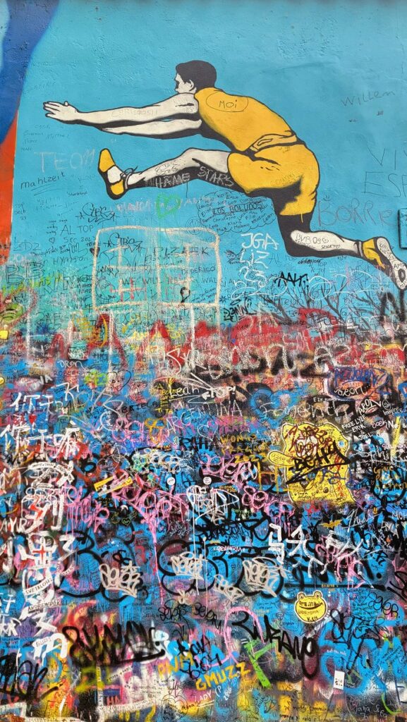 Track athlete jumping over all the graffiti on the Lennon Wall in Prague, Czech Republic