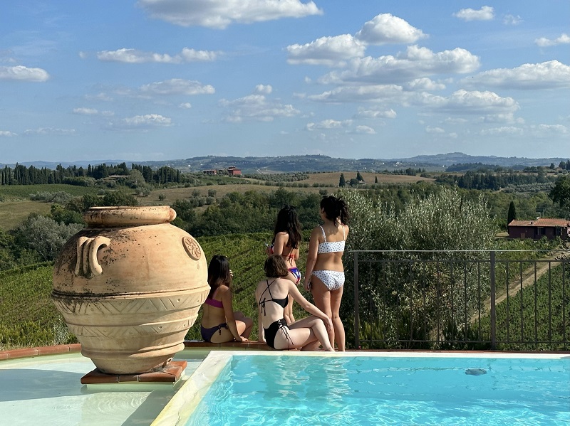 Brandeis Midyear in Florence students sitting at the edge of a pool looking out  at a vineyard in Villa Ilangi