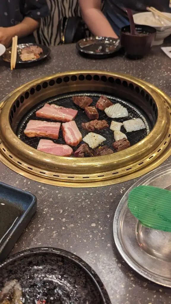 A grill in the middle of the table of yakiniku (all you can eat) of different cuts of meat