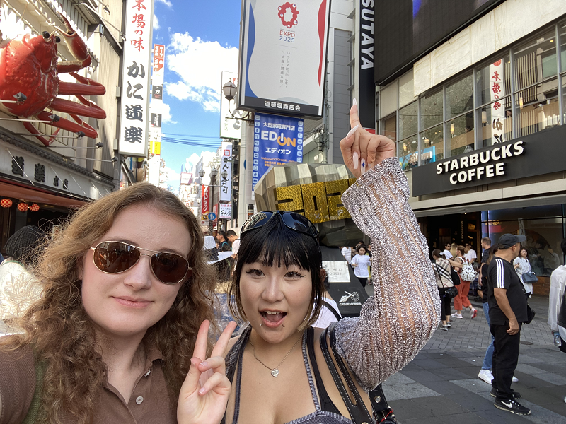 CET Japan student and her housemate standing in the street by an Expo 2025 poster in the city